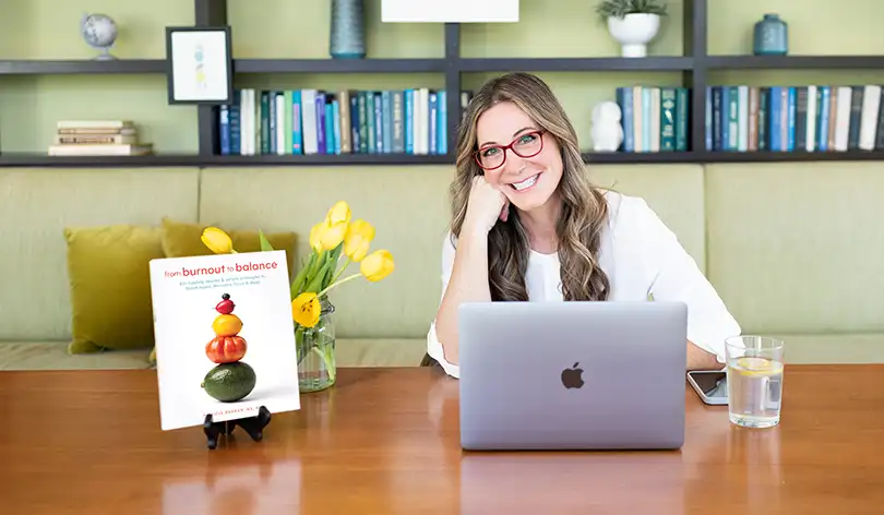 Patricia Bannan sitting at table with laptop and book From burnout to balance