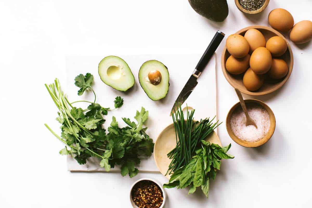 avocado egg boats ingredients with cilantro, herbs, eggs, and avocado