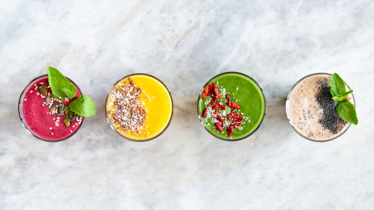 four different types of supercharged smoothies for beginners with different toppings and colors on a marble background