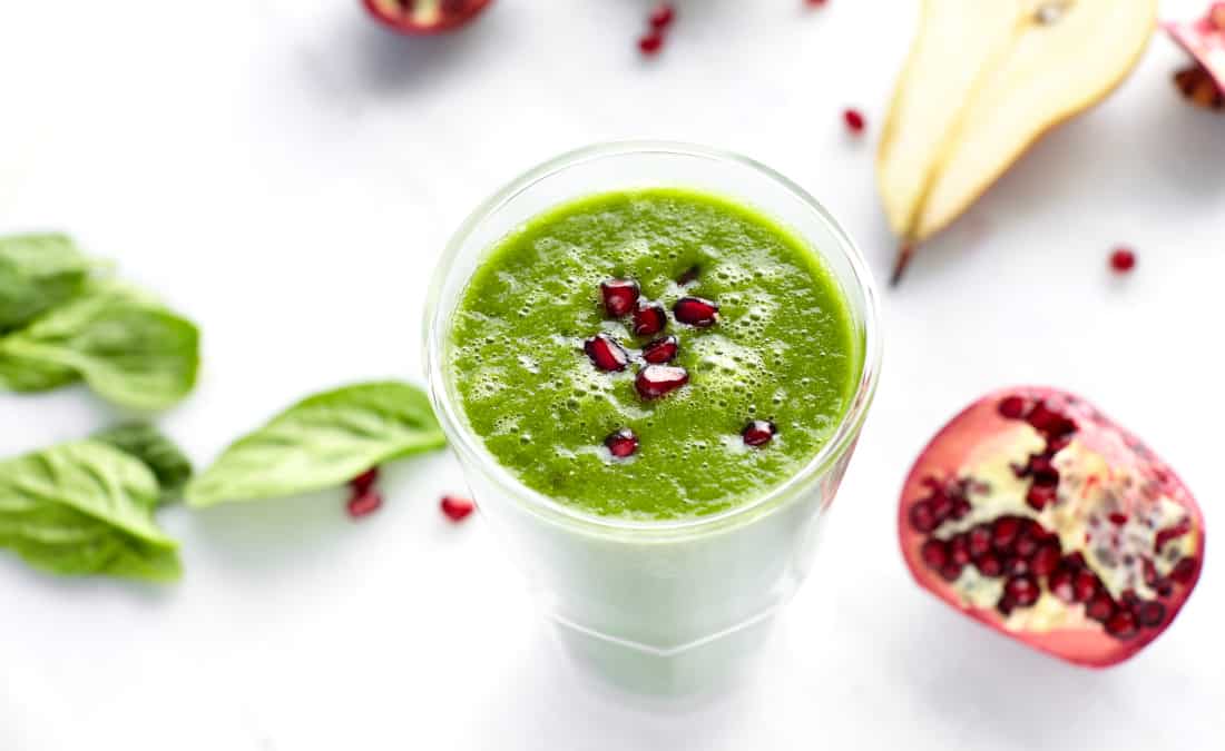 green smoothie with spinach, pomegranate, and pear on a white background