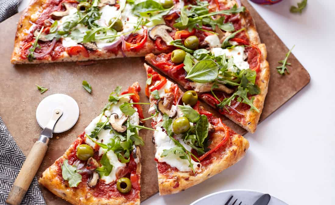 aerial view of homemade veggie pizza cut into pieces with wooden pizza cutter