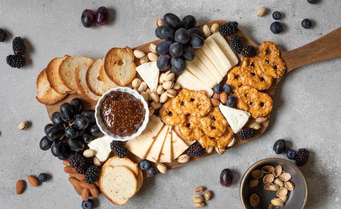 diy cheese board with different types of cheese, pretzels, crackers, fruit, and nuts