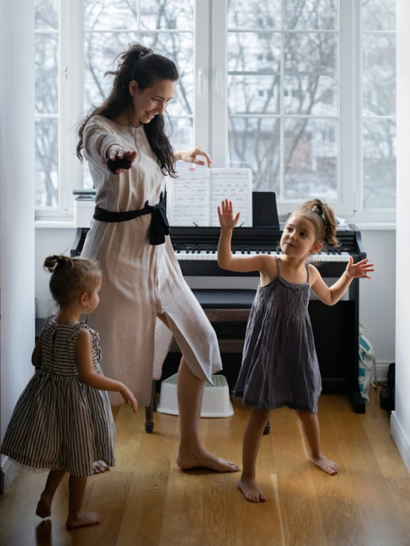 mom and daughters dancing together by piano for fun indoor activity